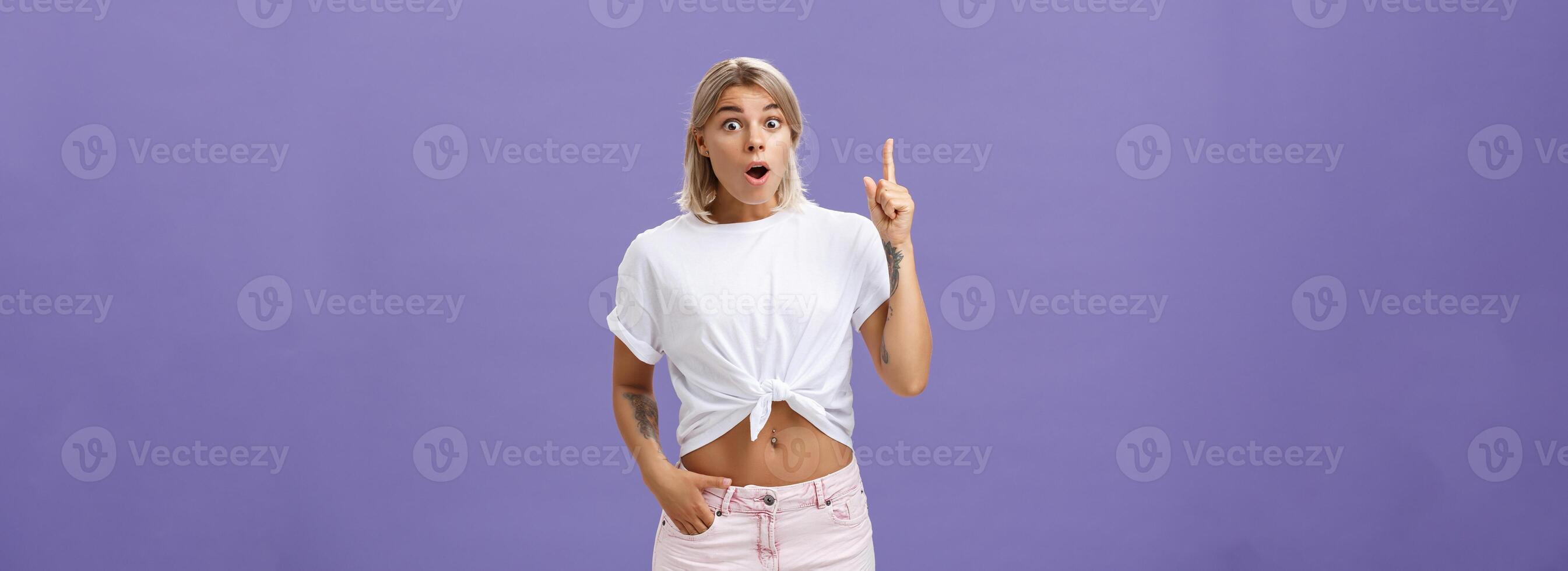 I have got idea. Thrilled and excited attractive stylish feminine woman with tattoos popping eyes folding lips, gasping raising index finger up in eureka gesture having excellent idea over purple wall photo