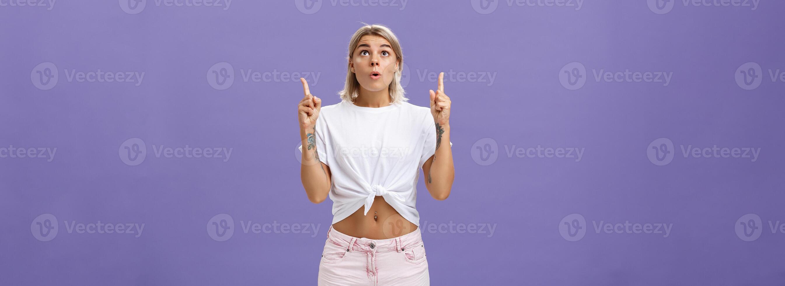 Girl dreaming become flight attendant being amazed with cool airplane flying in sky looking up with surprised impressed look saying wow pointing upwards posing over purple background photo