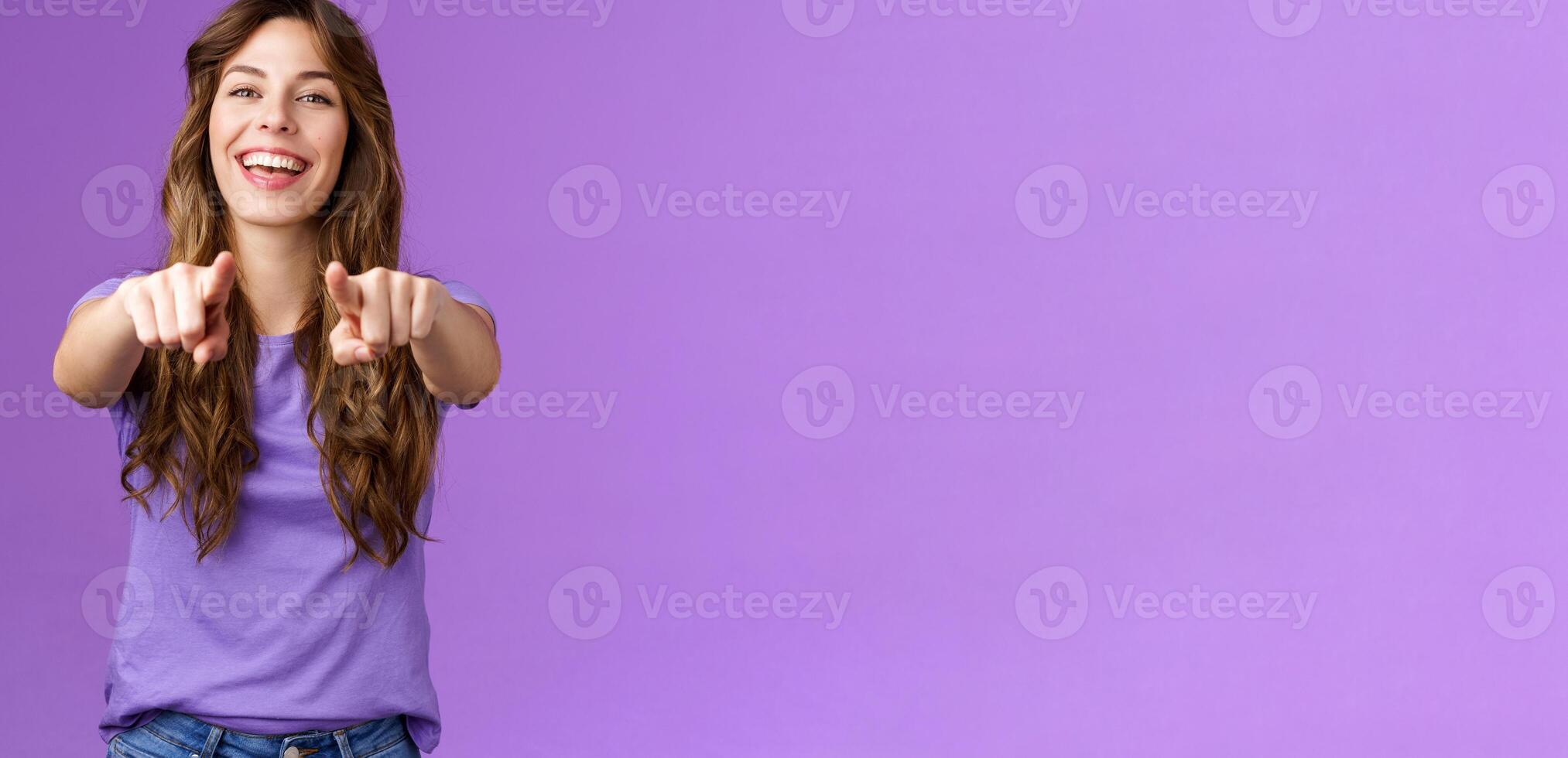 Its you. Friendly glad joyful happy curly-haired girl pointing fingers camera smiling broadly laughing congratulate friend singing song indicating boyfriend make choice stand purple background photo