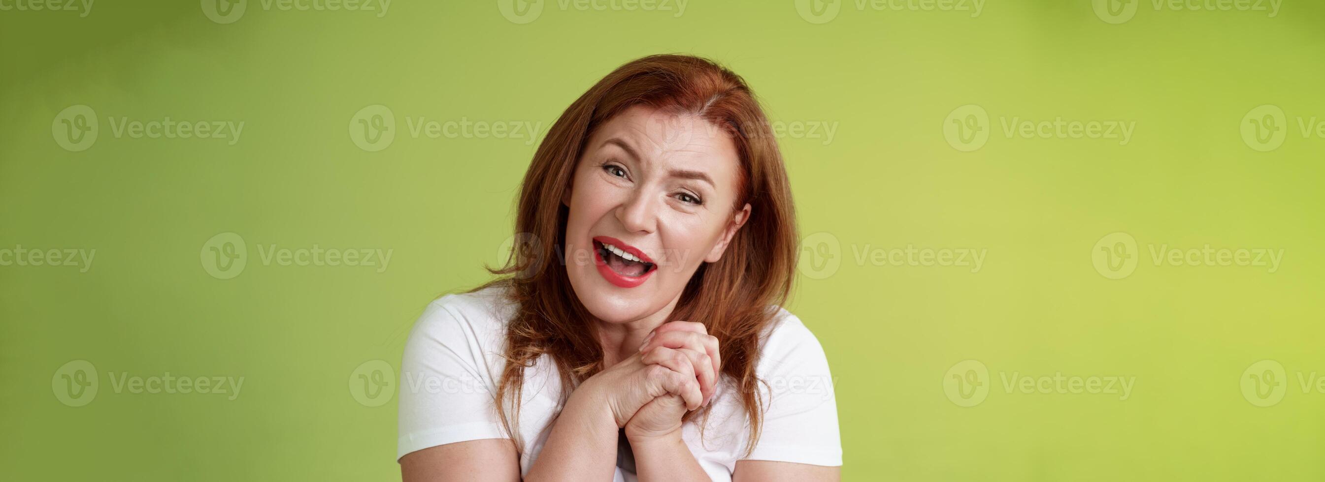 Close-yp touched tender kind redhead middle-aged granny sighing look admiration delight clasp hands heartwarming lovely scene smiling tilting head impressed satisfied stand green background photo