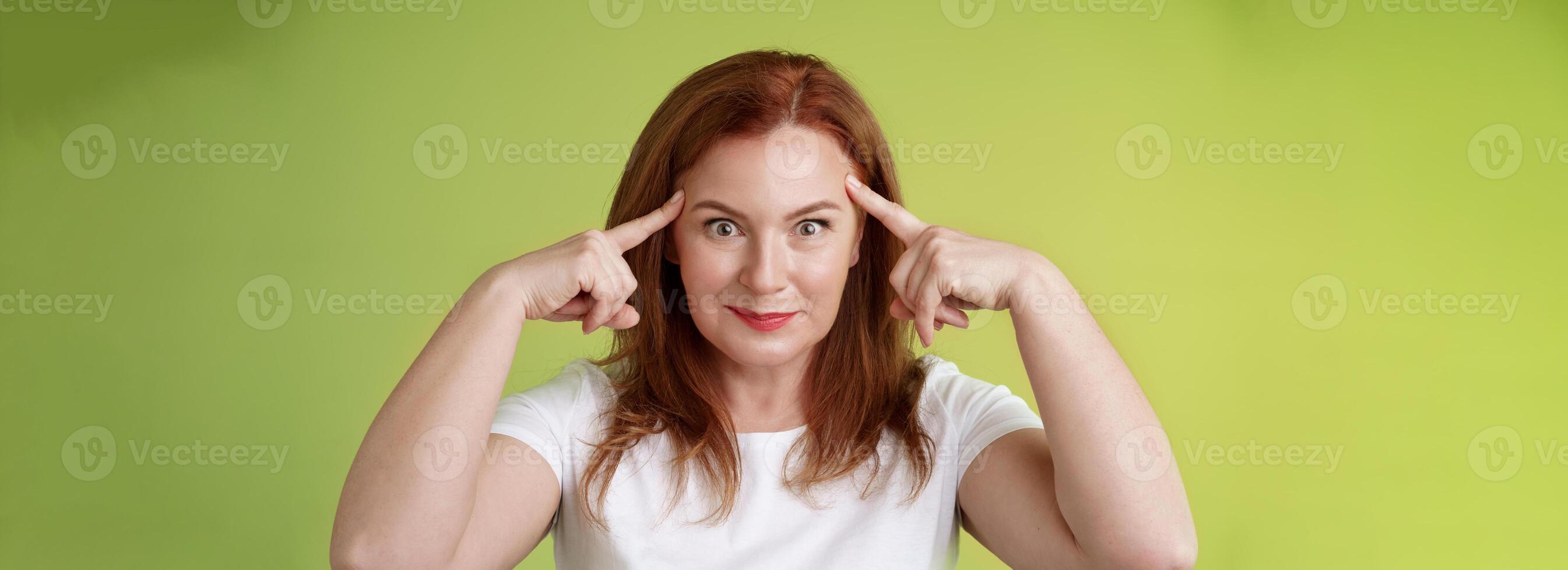 mujer en broma curioso gracioso controlar tu mente. tonto pelirrojo de edad mediana hembra toque templos estallar ojos sonriente Encantado leer pensamientos molesto adivinar intrigado qué pensando verde antecedentes foto