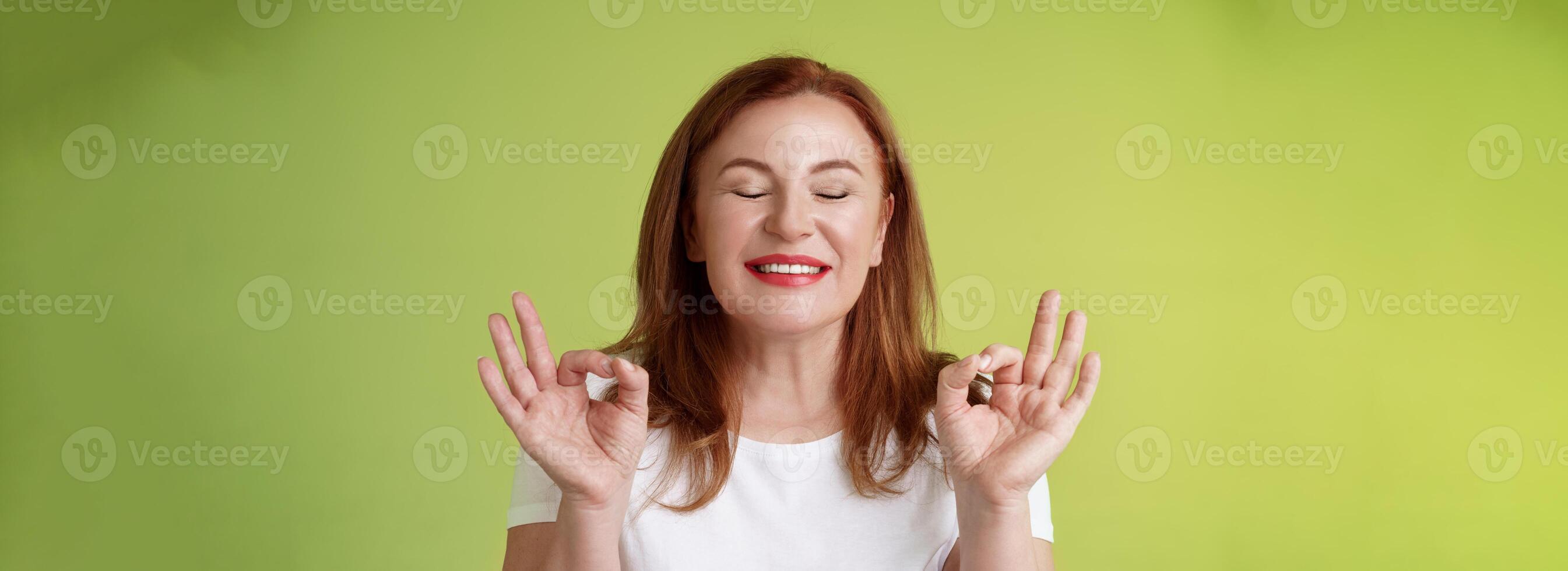 Close to perfection. Close-up peaceful relaxed redhead happy woman closed eyes pure delighted smile show zen peace satisfaction gesture meditating reach nirvana calm stand green background photo