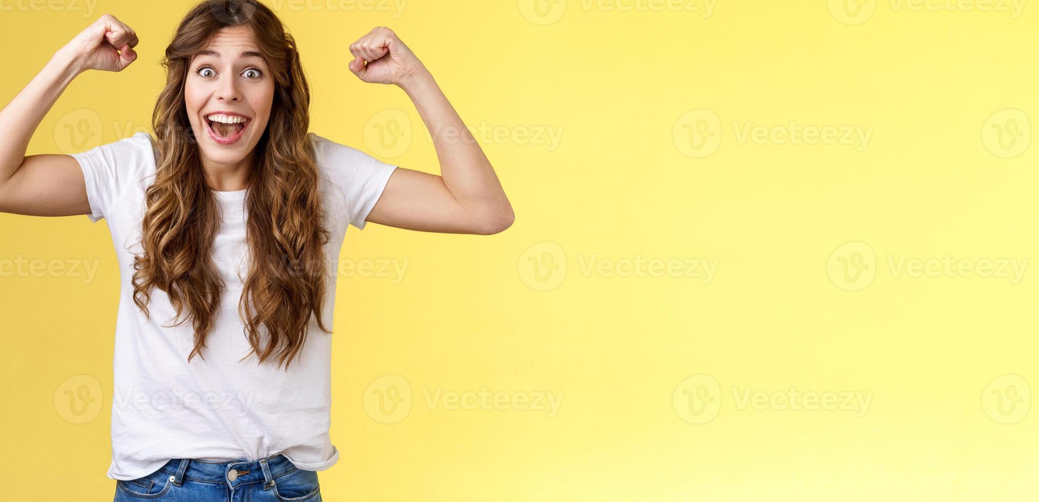 Lucky girl feeling like winner. Triumphing excited cheerful young woman raise hands fist pump up celebratory smiling broadly thrilled yelling supportive root favorite team reach success photo