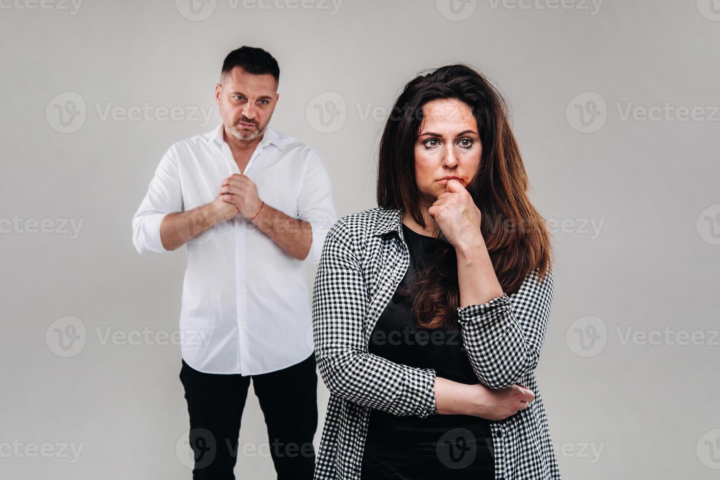 A woman beaten by her husband standing behind her and looking at her aggressively. Domestic violence photo