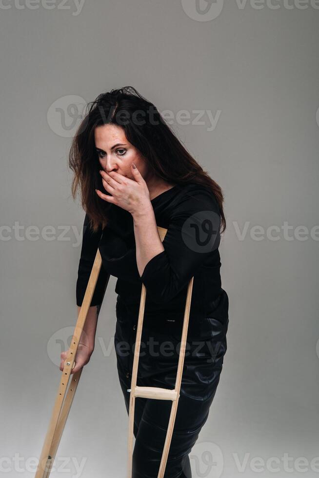 A woman beaten in black clothes with crutches in her hands on a gray background photo