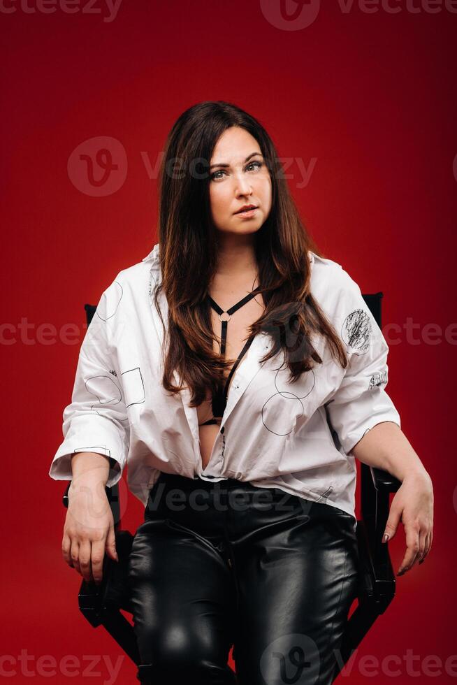 sexy mujer en un blanco camisa sentado en un negro silla en un rojo antecedentes foto