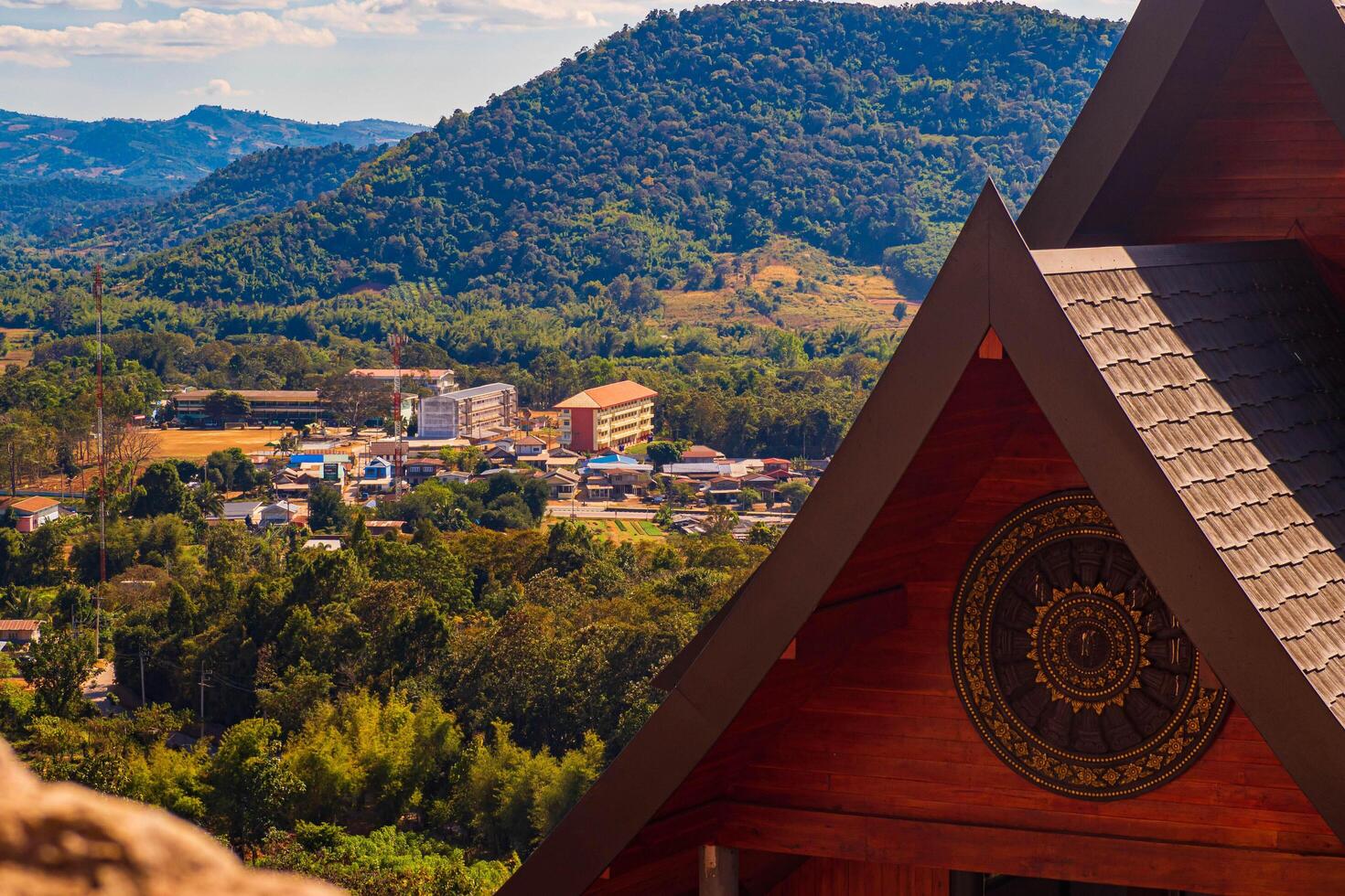 Loei, Thailand, 2023 - Aerial panorama with brown roof in foreground, there is a well-known tourist destination with views of the mountains, village, and a farm. photo