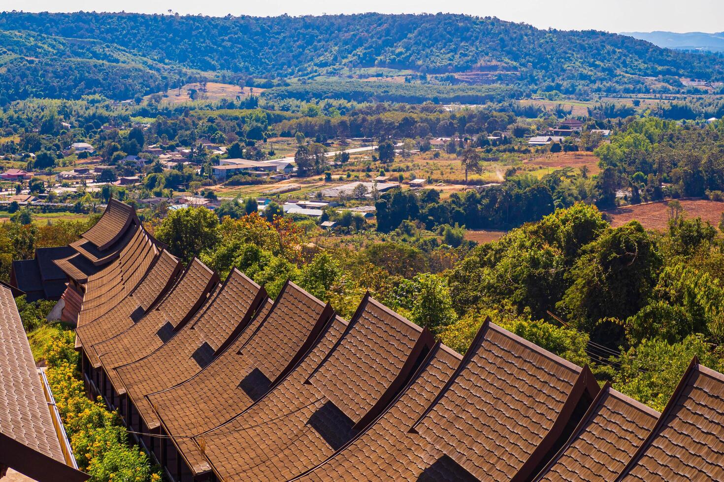 Loei, Thailand, 2023 - Aerial panorama with brown roof in foreground, there is a well-known tourist destination with views of the mountains, village, and a farm. photo