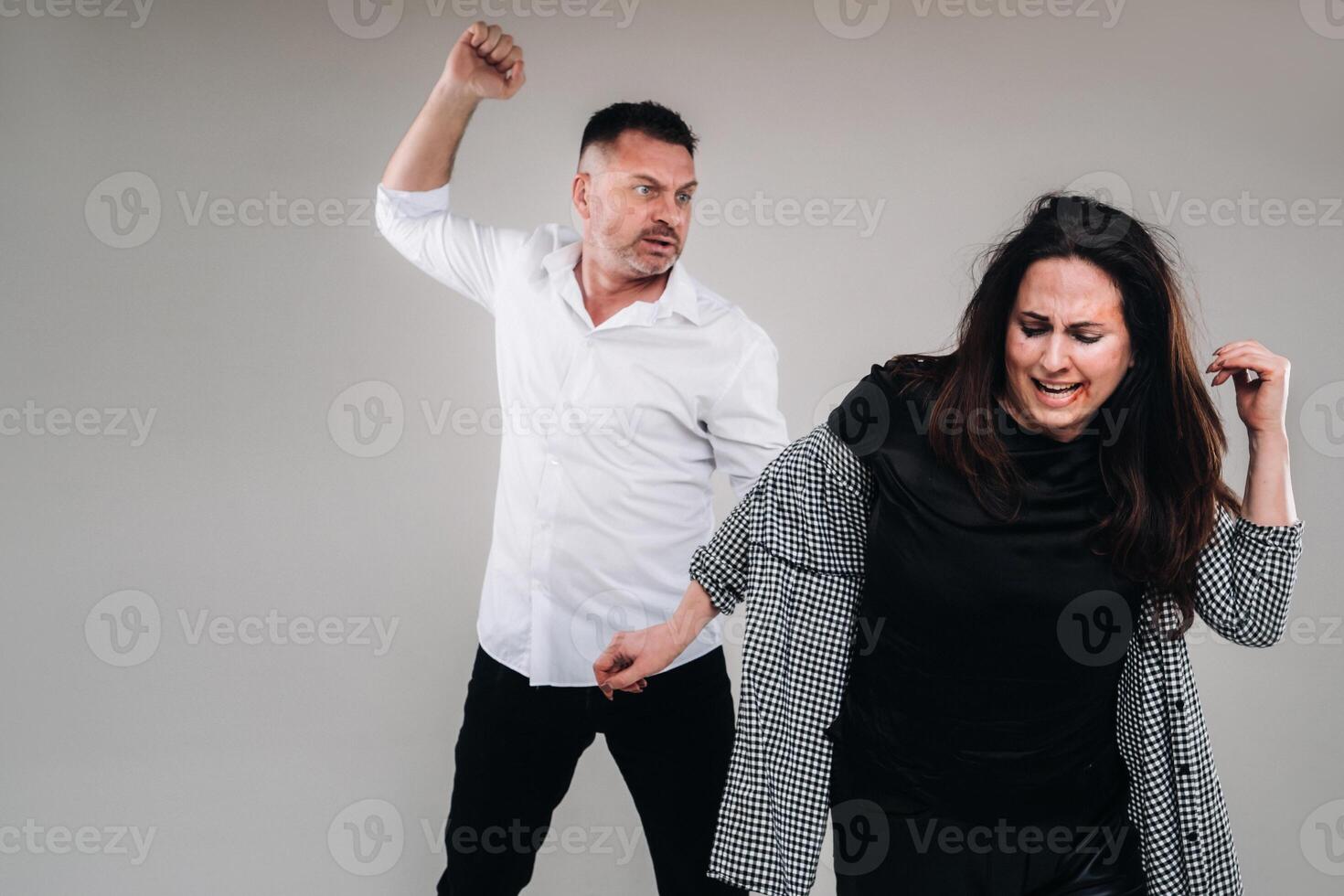 A man swings his hand at a battered woman standing on a gray background. Domestic violence photo