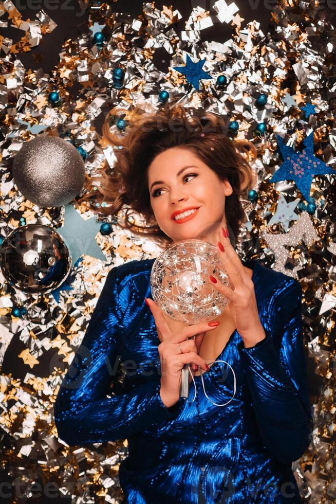 a woman in a blue sequined dress smiles and lies on the floor under a falling multicolored confetti photo