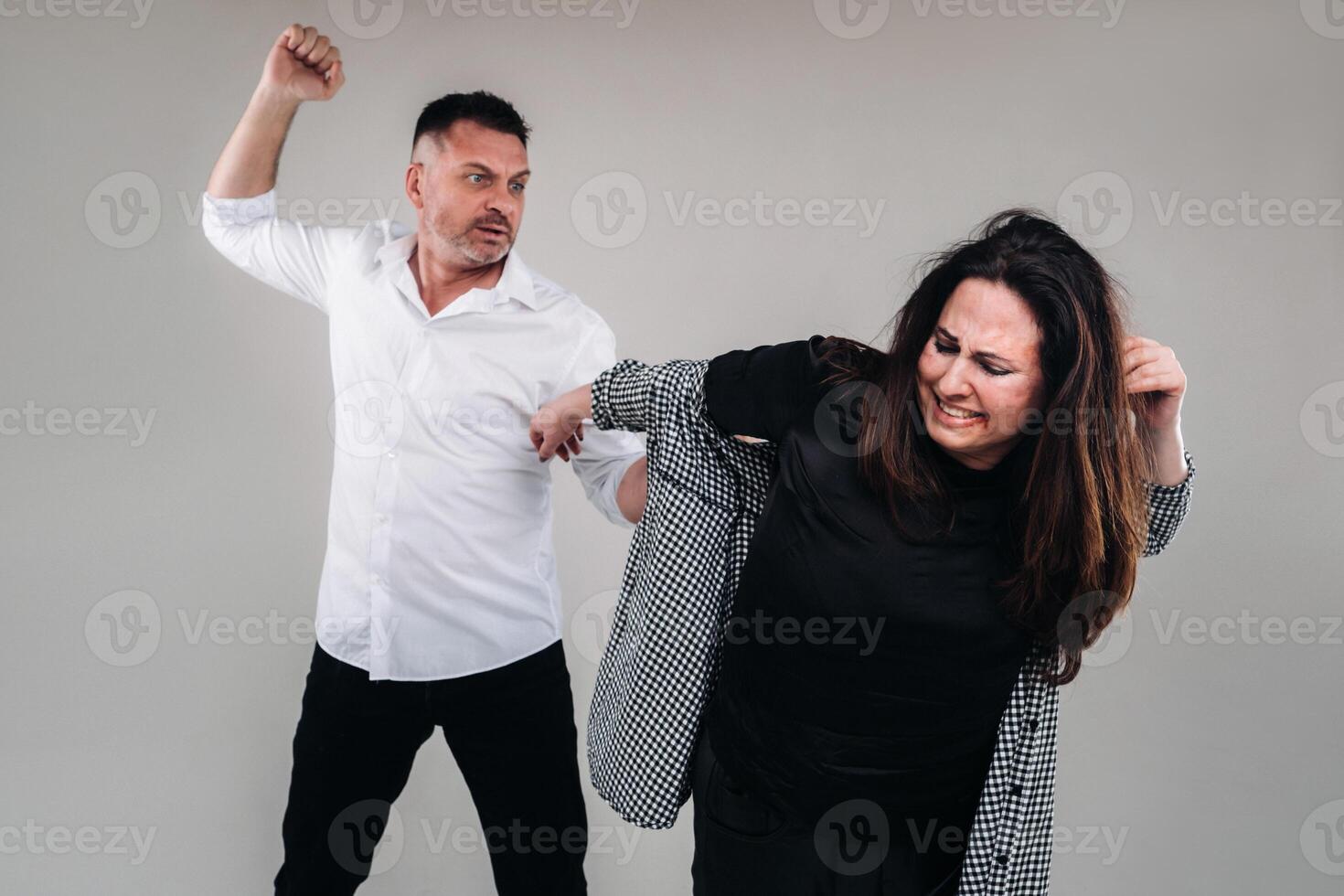 A man swings his fist at a battered woman standing on a gray background. Domestic violence photo