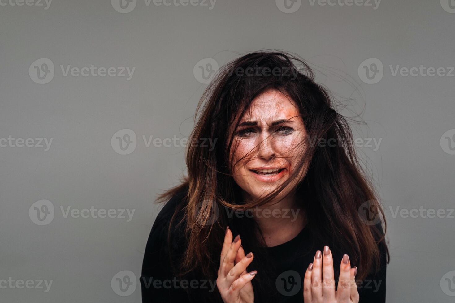 a battered woman in black clothes on an isolated gray background. Violence against women photo