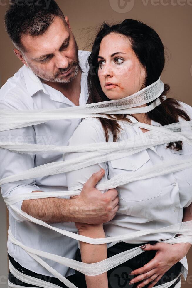 An aggressive man embraces a battered woman and is wrapped in bandages together. Domestic violence photo