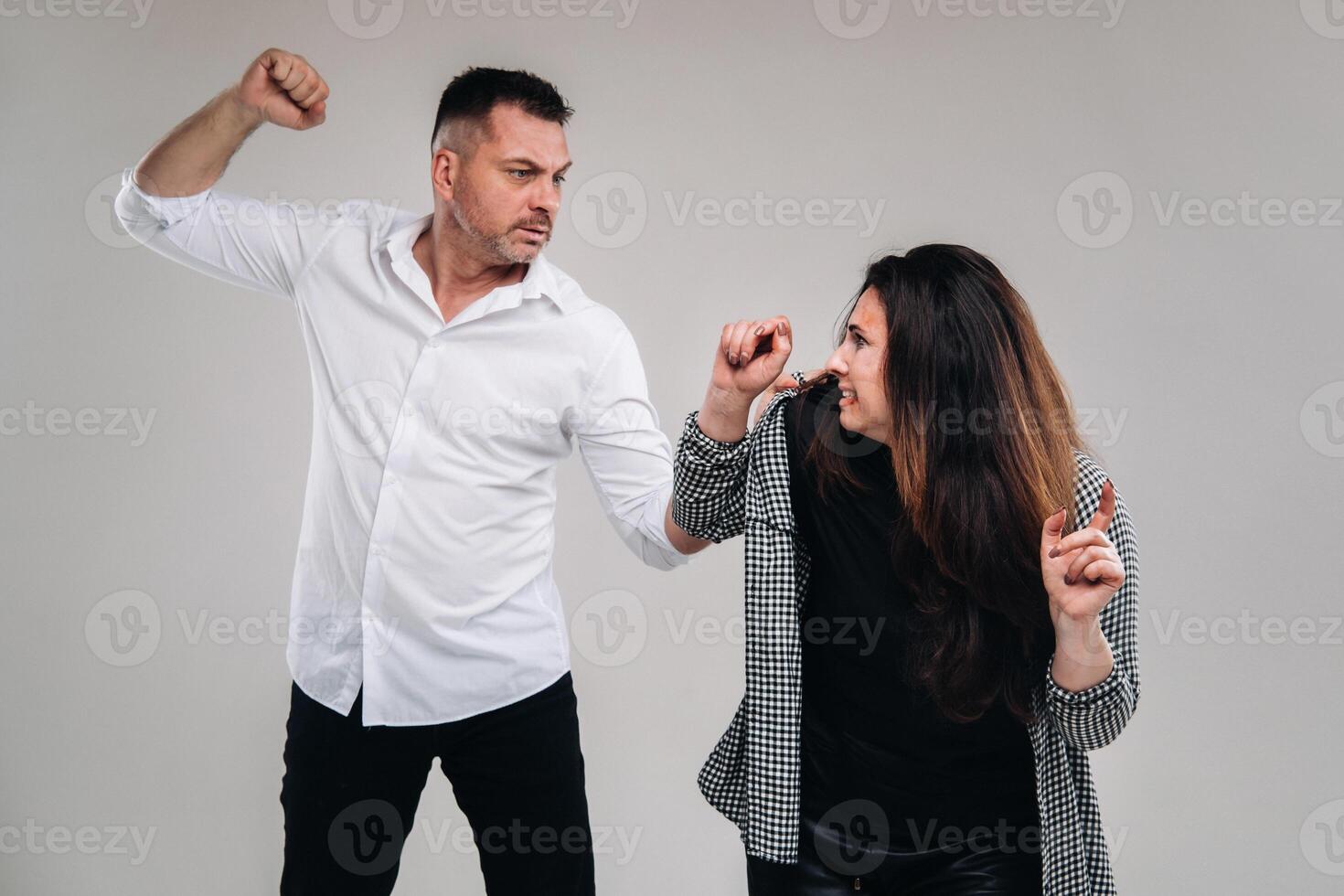 A man swings his fist at a battered woman standing on a gray background. Domestic violence photo