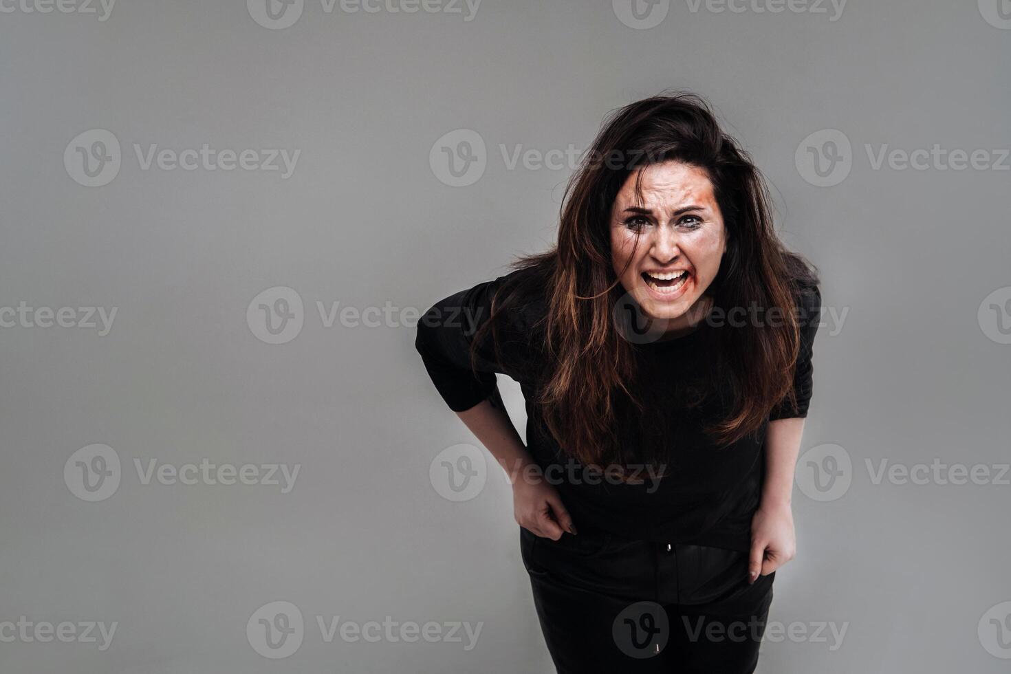a battered woman in black clothes on an isolated gray background. Violence against women photo