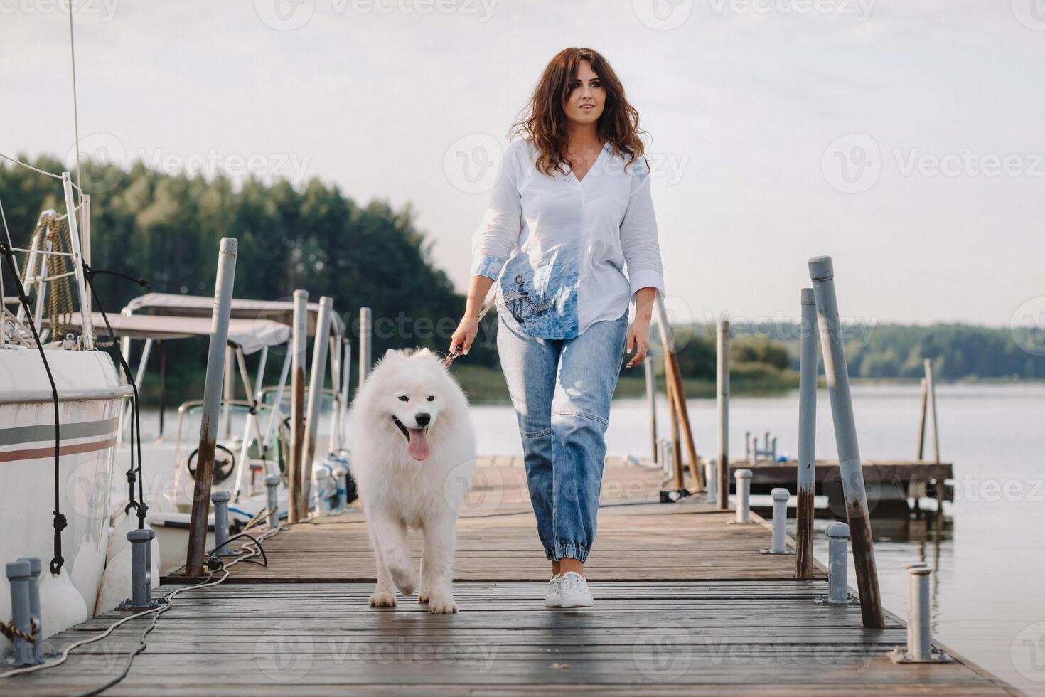 un contento mujer con un grande blanco perro camina en el muelle cerca el yate y el mar foto