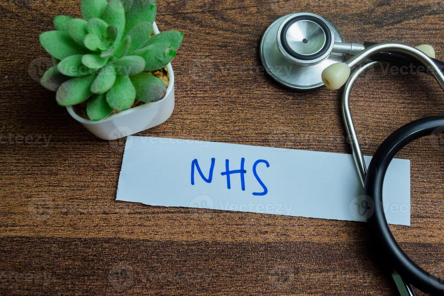 Concept of NHS write on sticky notes with stethoscope isolated on Wooden Table. photo