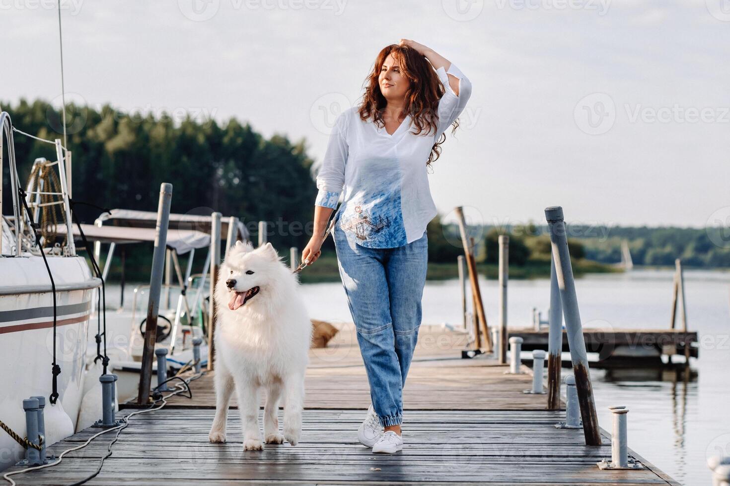 un contento mujer con un grande blanco perro camina en el muelle cerca el yate y el mar foto