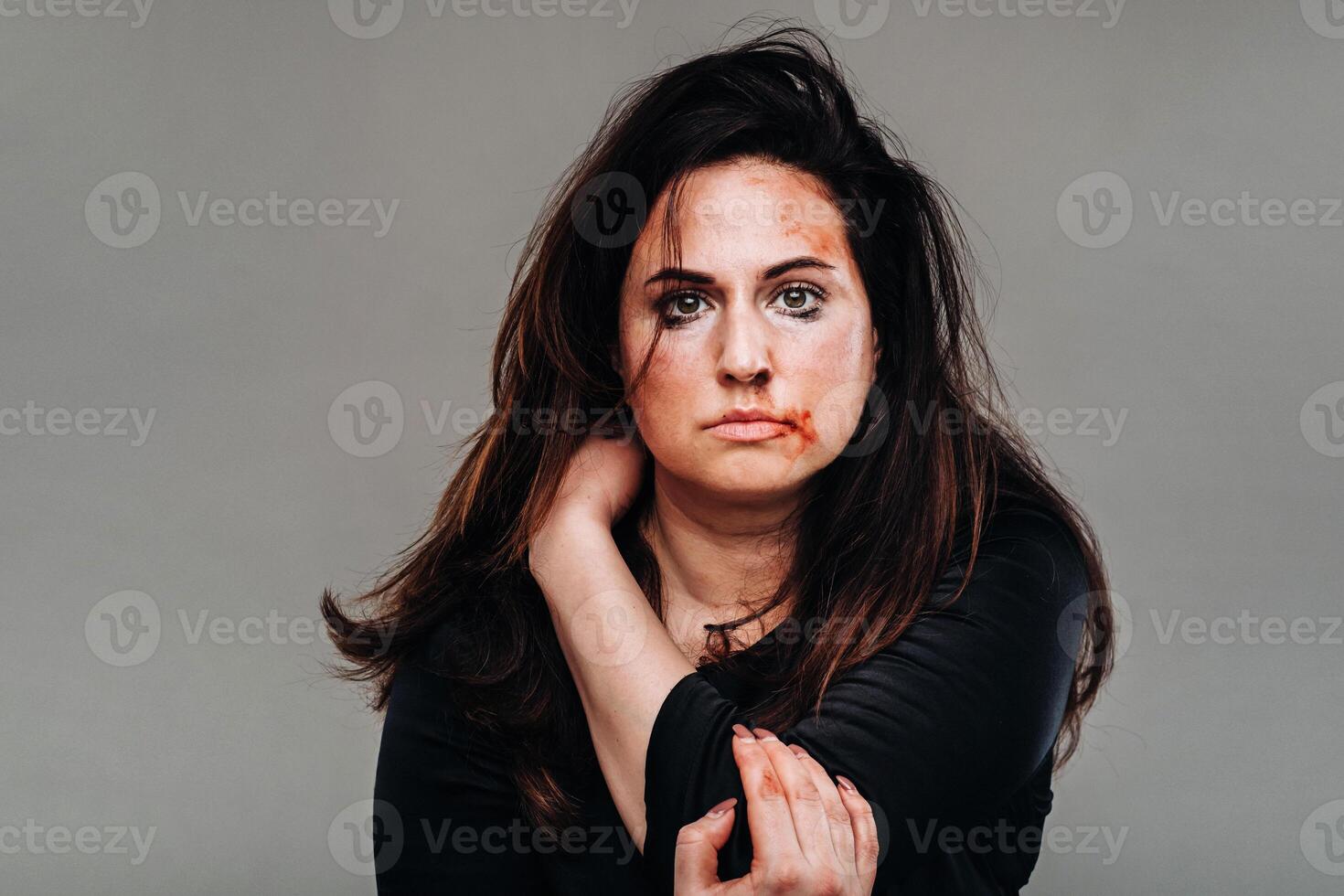 a battered woman in black clothes on an isolated gray background. Violence against women photo