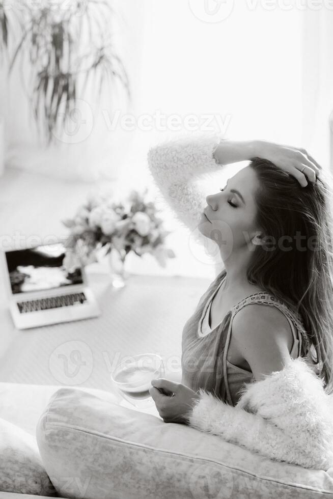 un relajado niña a hogar bebidas café y relojes un pelicula.domestica calma.la niña es sentado cómodamente en el sofá y Bebiendo cafe.negro y blanco foto