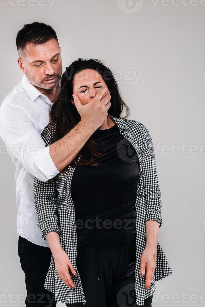 An aggressive man covers the mouth of a beaten woman so that she cannot scream. Domestic violence photo