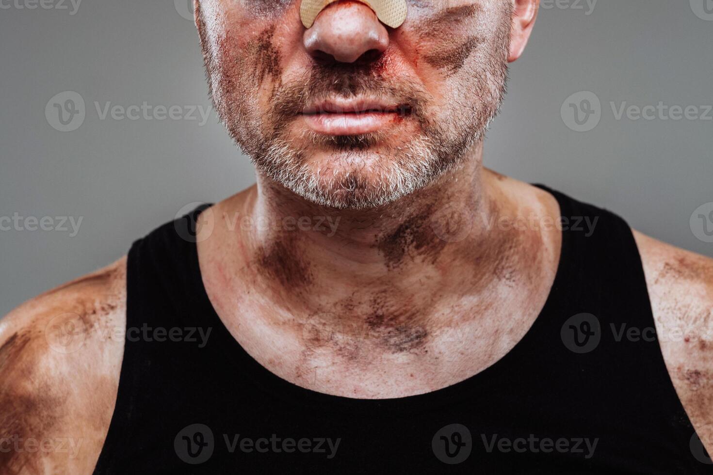 a battered man in a black T shirt who looks like a drug addict and a drunk stands against a gray background photo