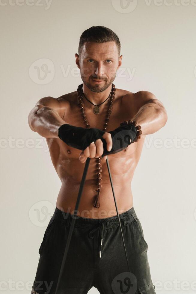 A man with a naked torso is engaged in strength fitness using a rubber loop indoors photo