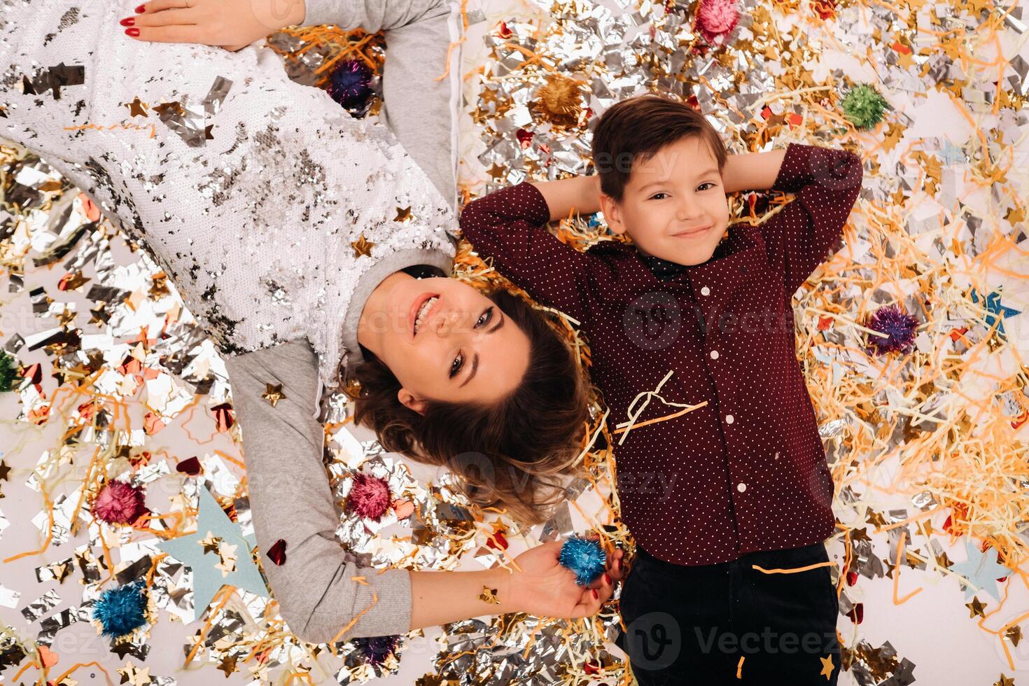 mother and son lie on the floor in confetti on a white background. A woman and a boy in confetti on a white background photo