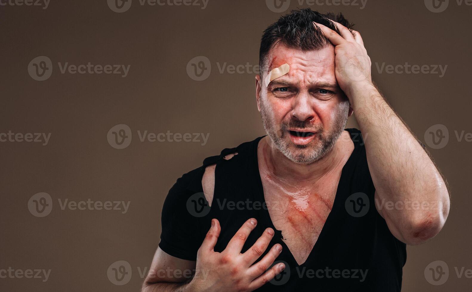 Against a gray background stands a battered angry man in a black T-shirt with wounds photo