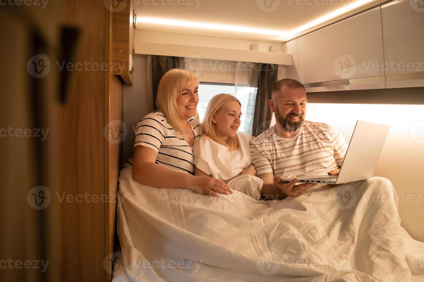 A family of three is watching a movie on a laptop while sitting in the bed of their motorhome photo
