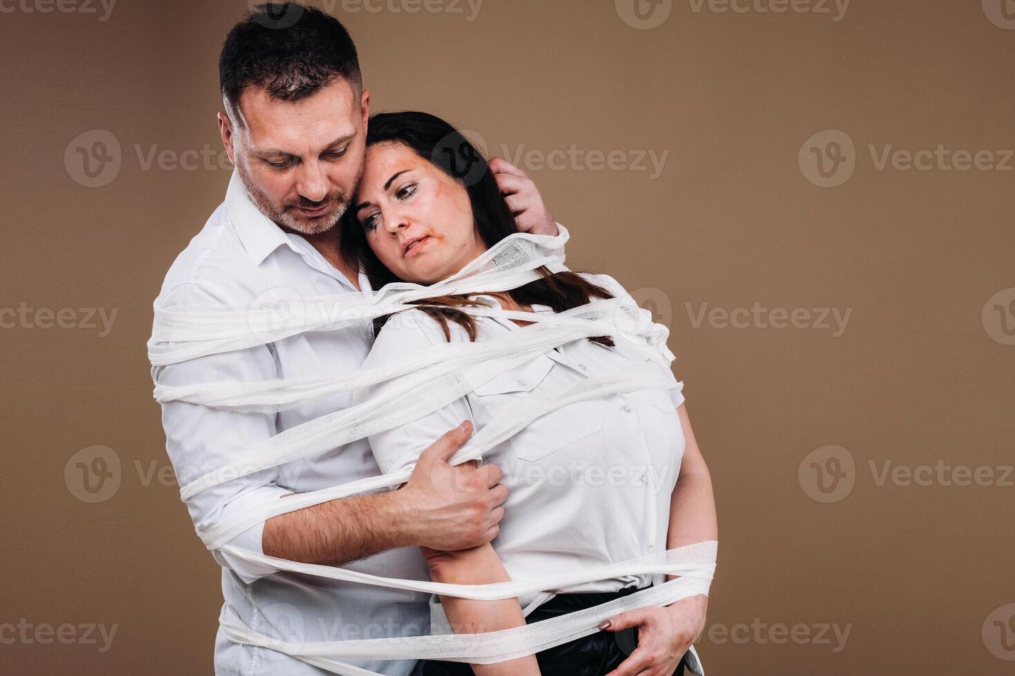 un agresivo hombre abraza un abollado mujer y es envuelto en vendajes juntos. Doméstico violencia foto