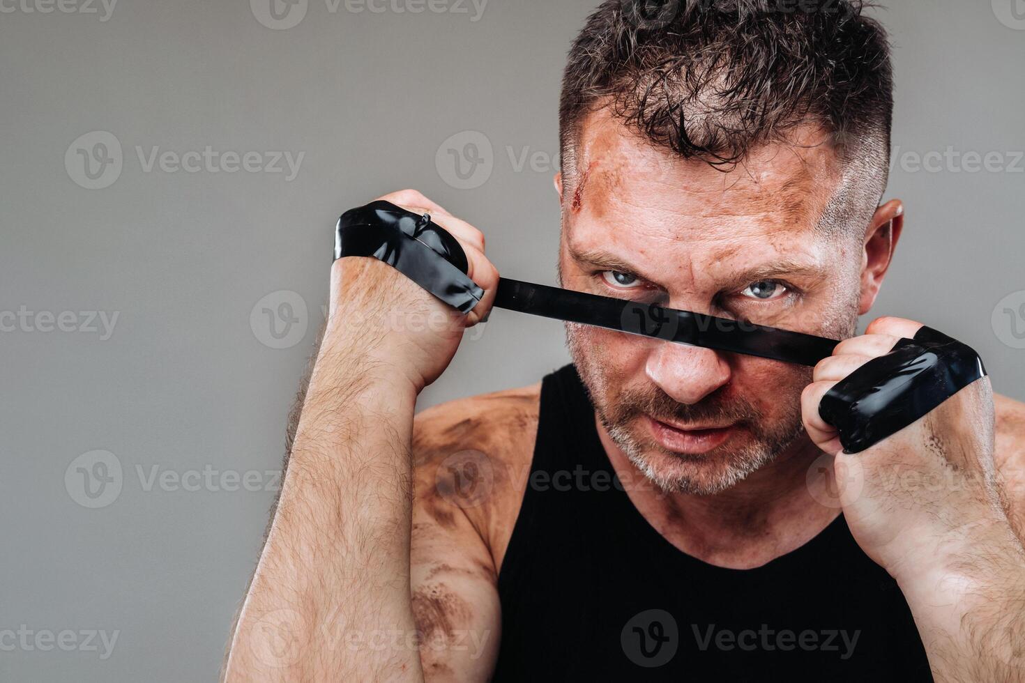 on a gray background stands a battered man in a black T shirt looking like a fighter and preparing for a fight photo