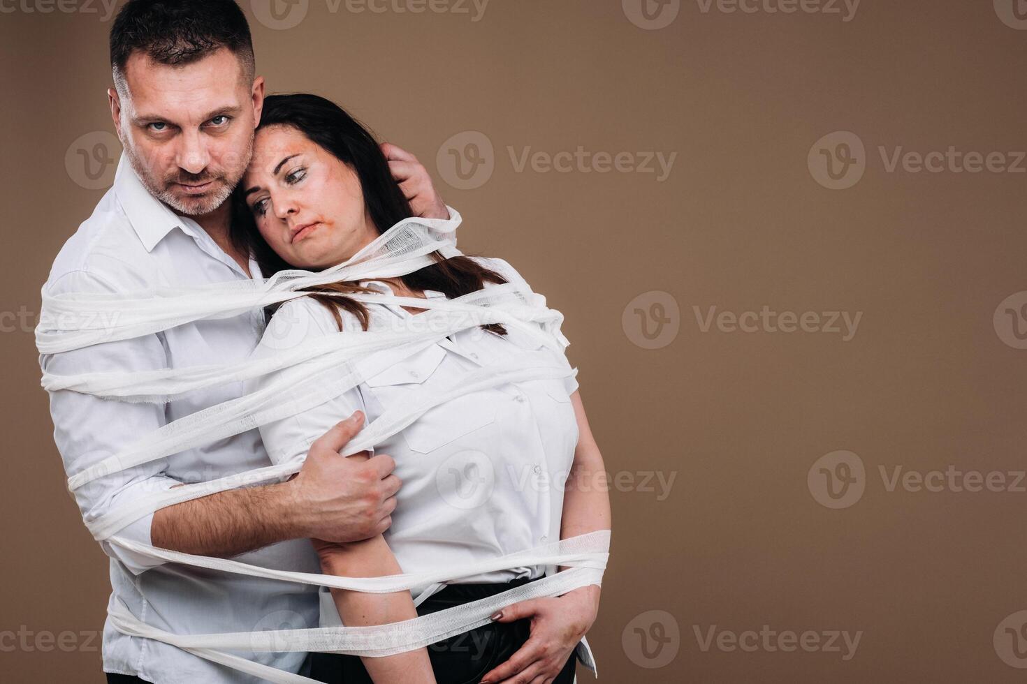 un agresivo hombre abraza un abollado mujer y es envuelto en vendajes juntos. Doméstico violencia foto