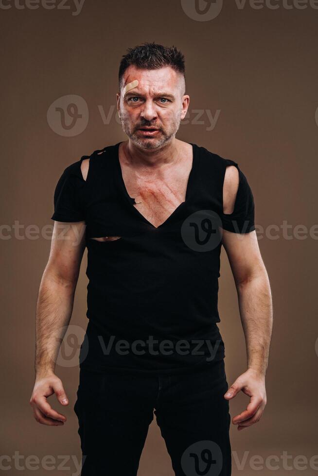 Against a gray background stands a battered angry man in a black T-shirt with wounds photo