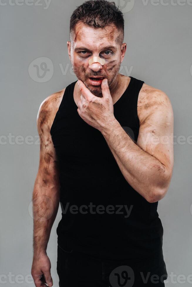 a battered man in a black T shirt who looks like a drug addict and a drunk stands against a gray background photo