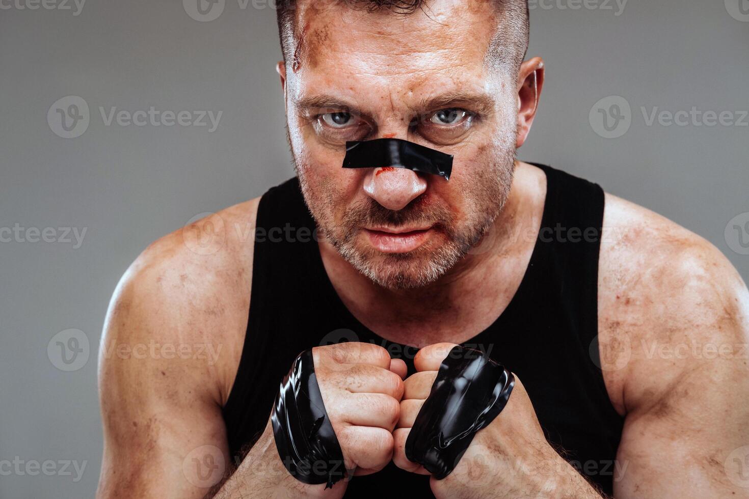 on a gray background stands a battered man in a black T shirt looking like a fighter and preparing for a fight photo