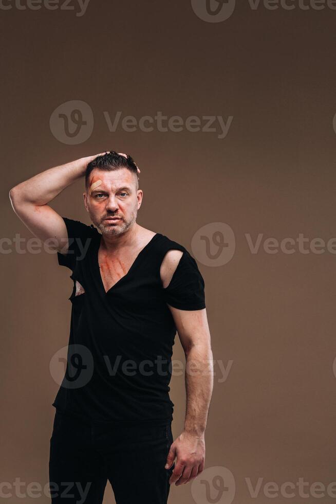 Against a gray background stands a battered angry man in a black T-shirt with wounds photo