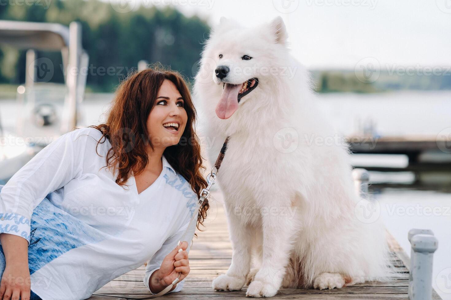 a happy woman with a big white dog lies on a pier near the sea at sunset photo