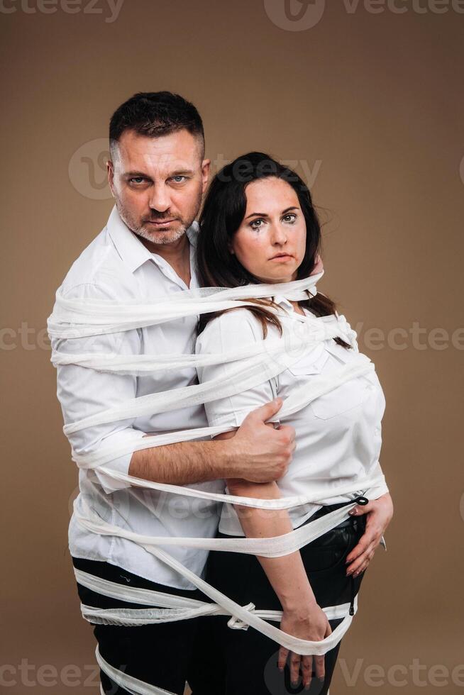 An aggressive man embraces a battered woman and is wrapped in bandages together. Domestic violence photo