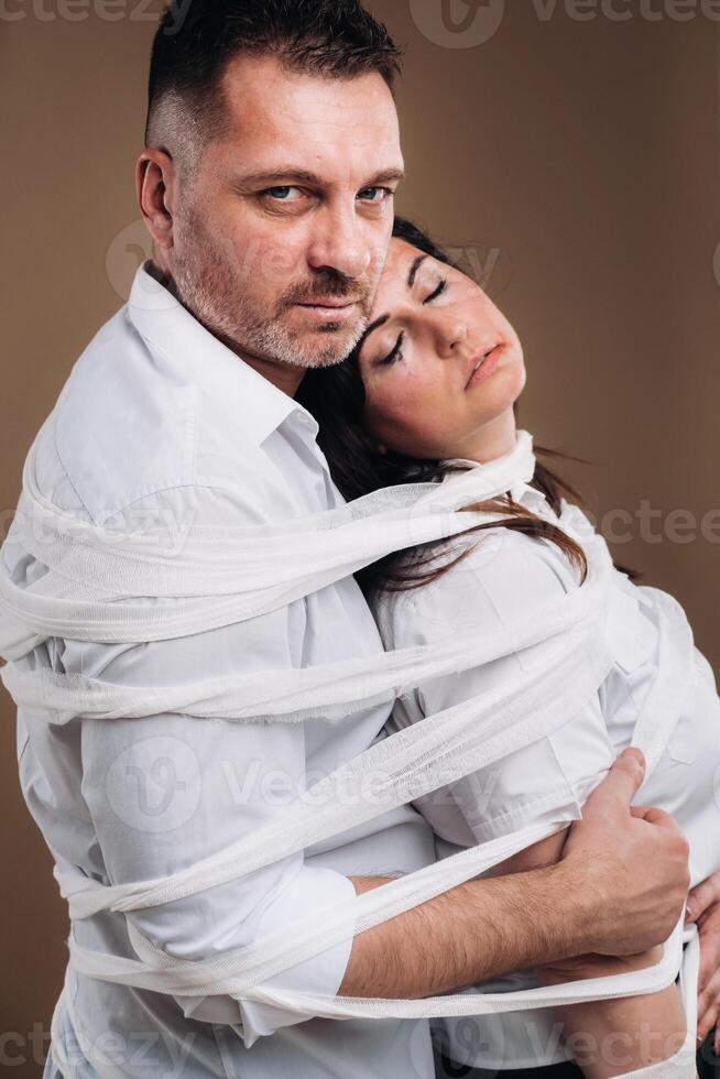 An aggressive man embraces a battered woman and is wrapped in bandages together. Domestic violence photo