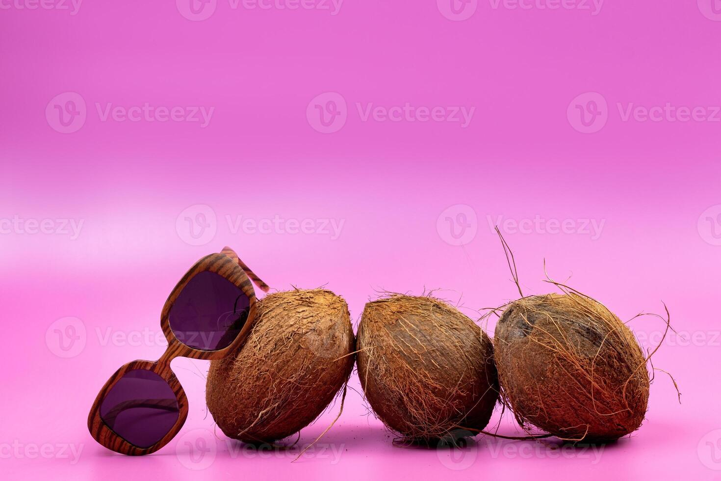 three whole coconuts and wooden glasses on a pink background photo