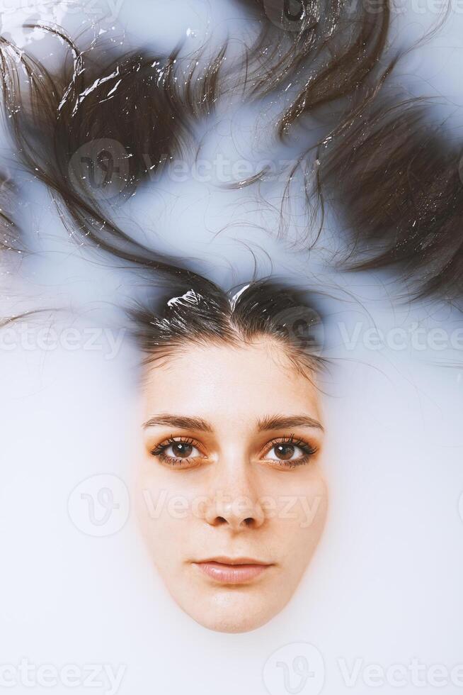 beauty portrait of young woman face and hair floating in milk bath photo