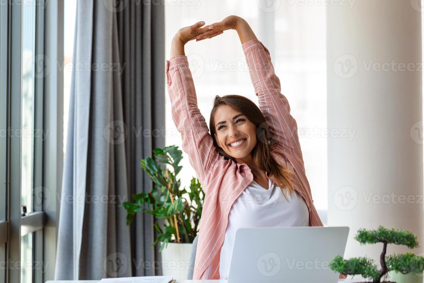 Young woman working on laptop. Business woman busy working on laptop streching. Businesswoman sitting at bright modern work station photo