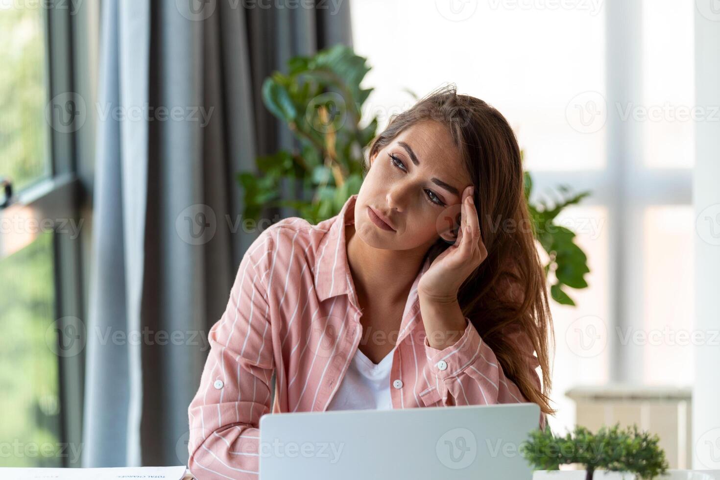 Young woman tired, exhausted from working studying hard. Bored and frustrated looking at laptop. Head resting on hand. Bright space big windows. At home concept. Stress concept. photo