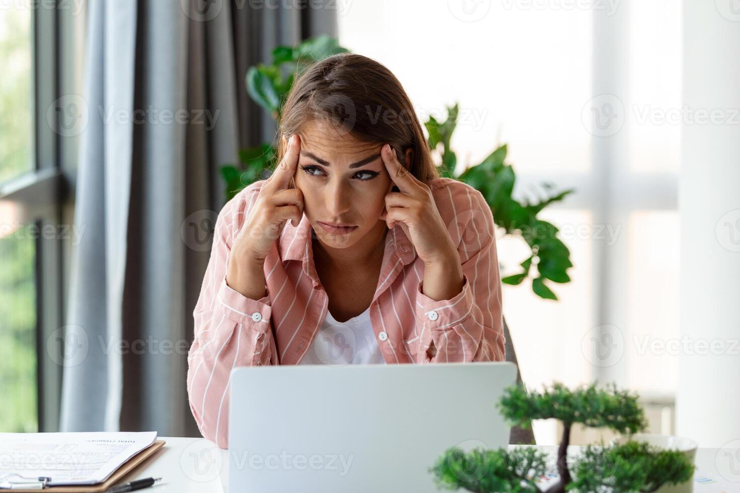 Young woman tired, exhausted from working studying hard. Bored and frustrated looking at laptop. Head resting on hand. Bright space big windows. At home concept. Stress concept. photo