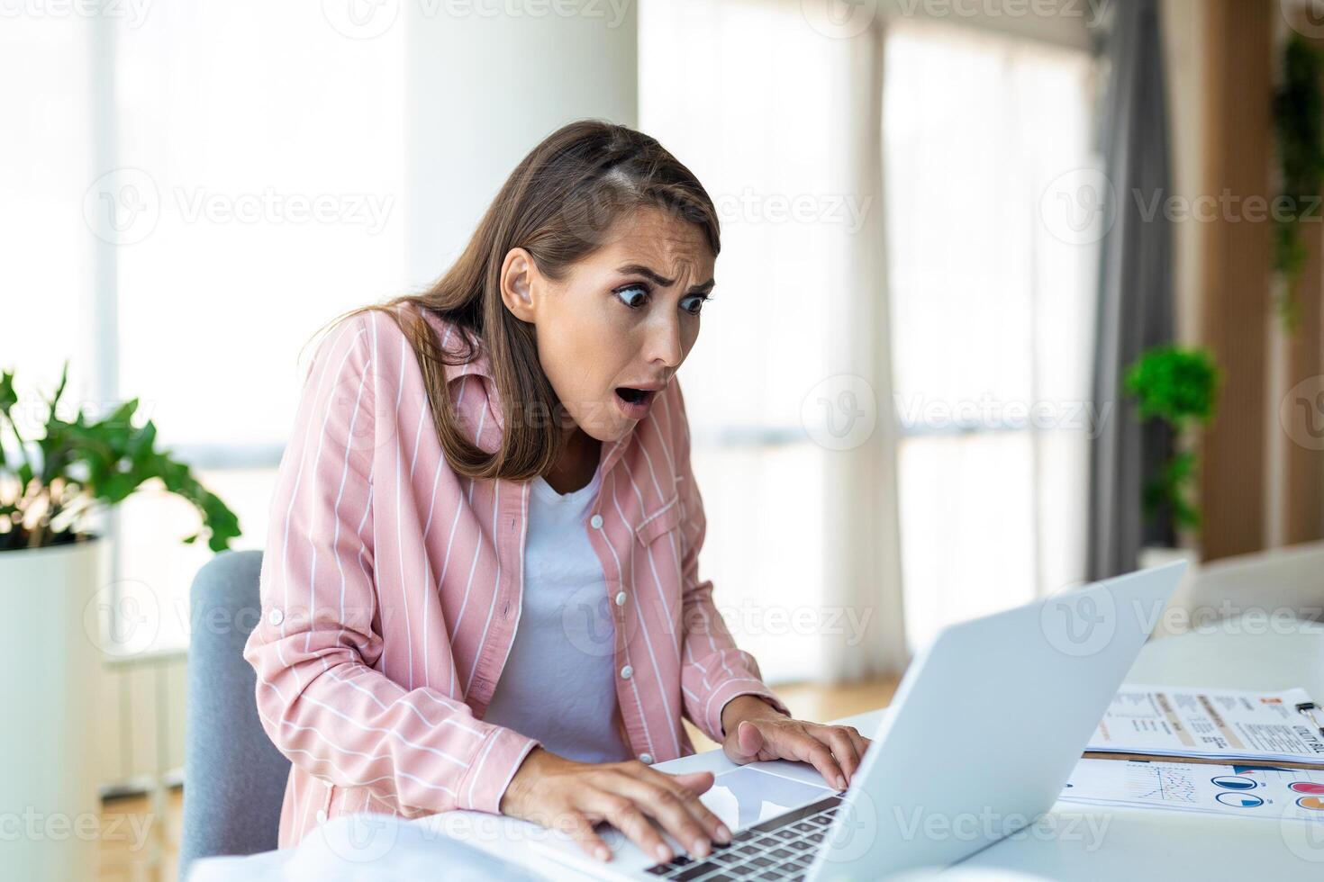 Shocked woman , exhausted from working studying hard. Bored and frustrated looking at laptop. Head resting on hand. Bright space big windows. At home concept. Stress concept. photo