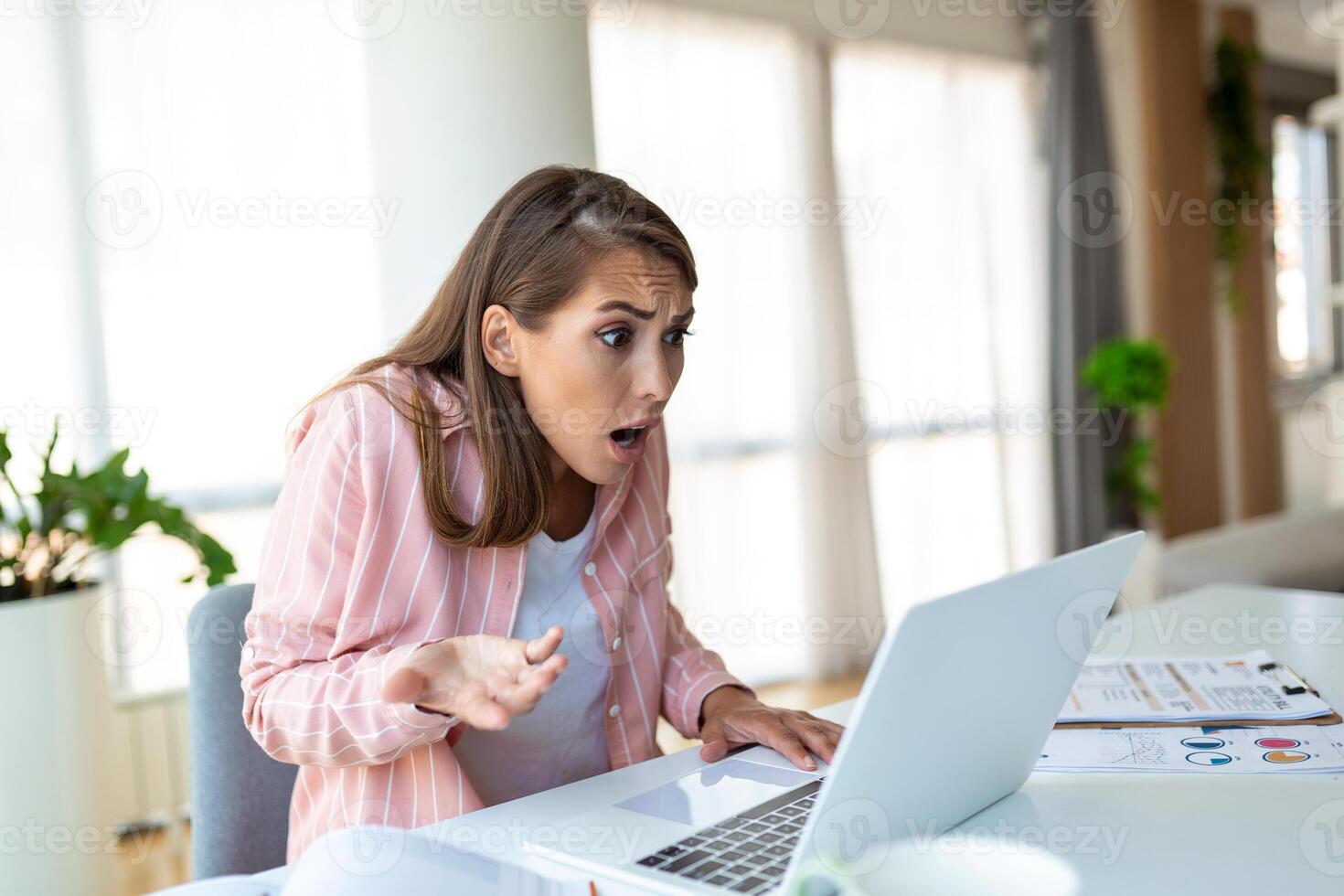 Shocked woman , exhausted from working studying hard. Bored and frustrated looking at laptop. Head resting on hand. Bright space big windows. At home concept. Stress concept. photo