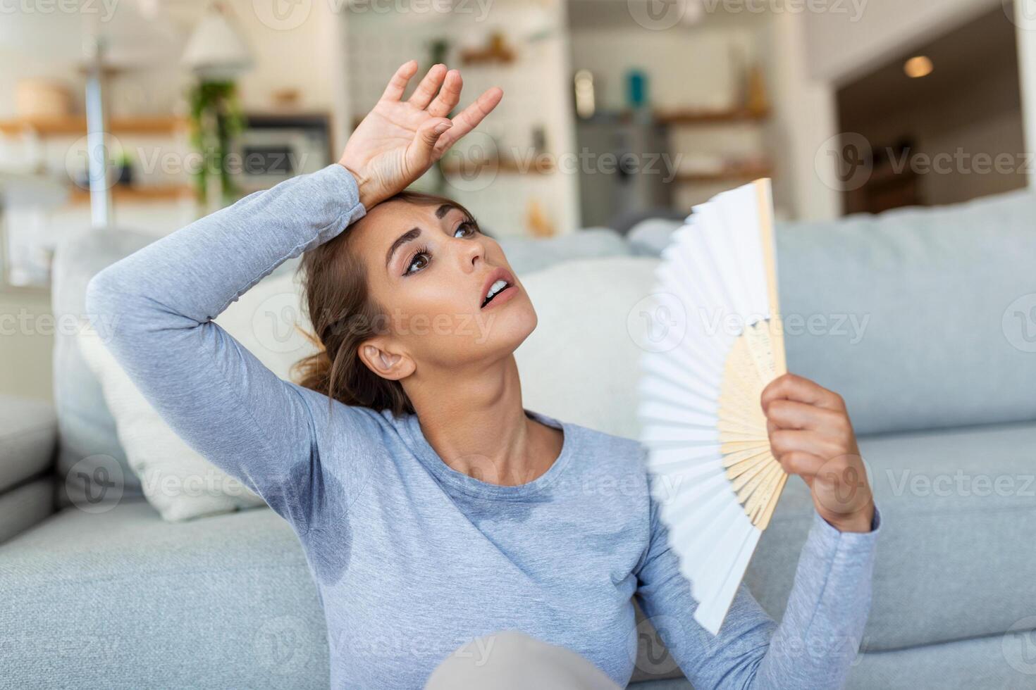 Woman puts head on sofa cushions feels sluggish due unbearable heat, waves hand fan cool herself, hot summer flat without air-conditioner climate control system concept photo