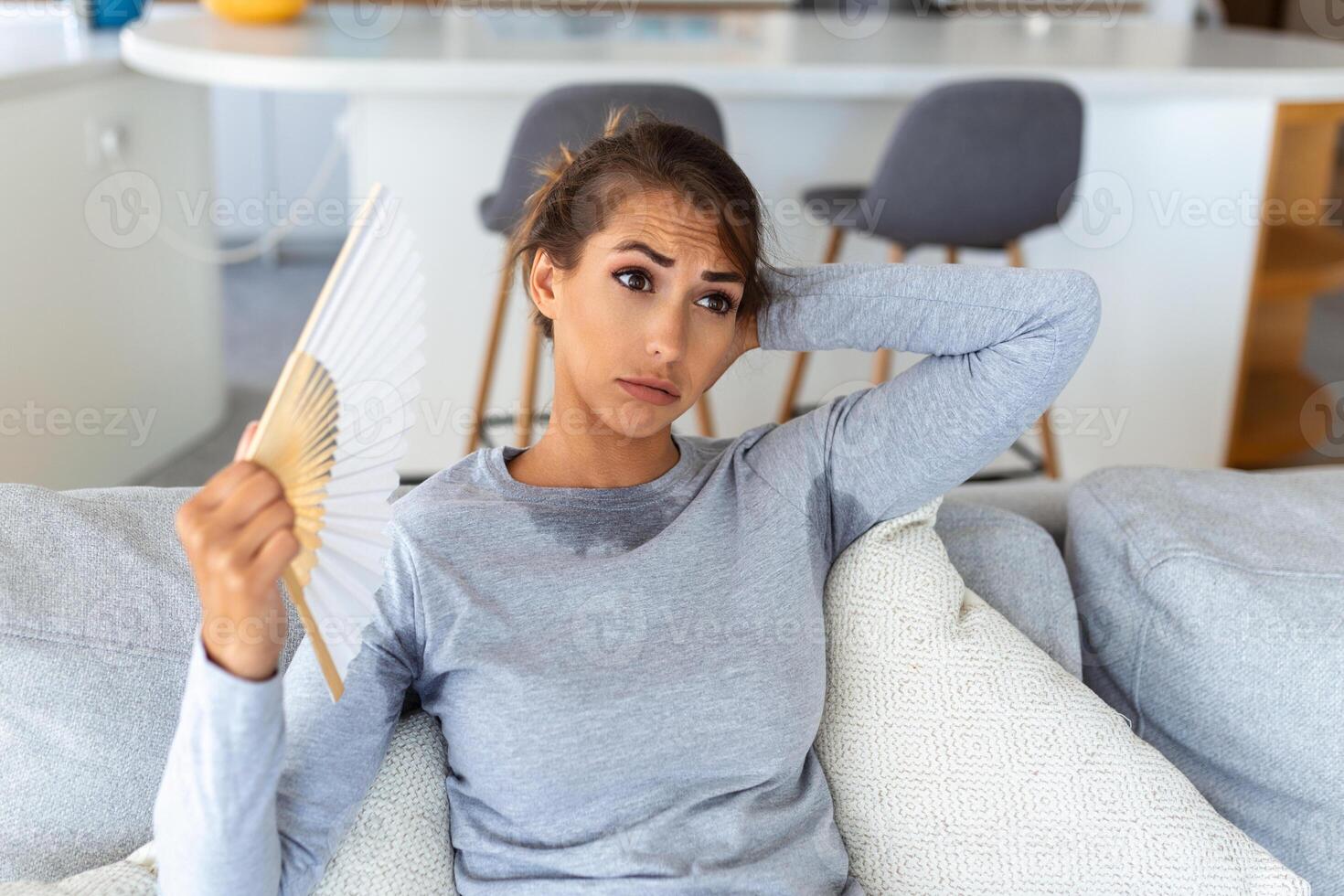 Woman puts head on sofa cushions feels sluggish due unbearable heat, waves hand fan cool herself, hot summer flat without air-conditioner climate control system concept photo