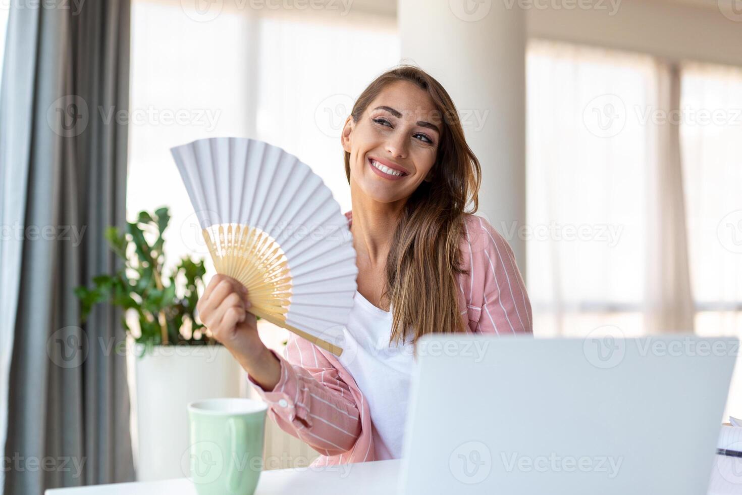 Tired overheated young woman hold wave fan suffer from heat sweating indoor work on laptop at home office, annoyed woman feel uncomfortable hot summer weather problem no air conditioner concept photo